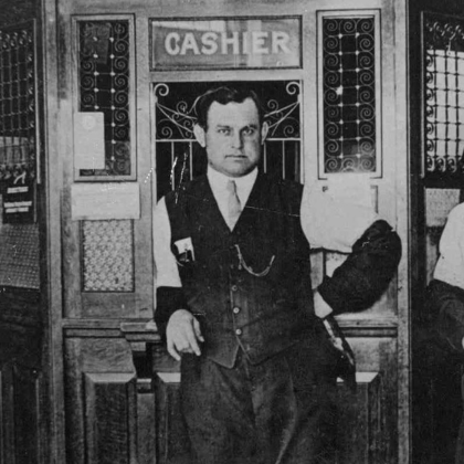 Image of JC Hamilton standing in front of cashier station (early 1900s)