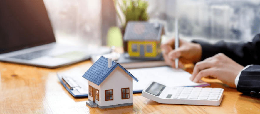 A man in a suit sits at a table with a calculator and laptop going through the process of a home loan application.