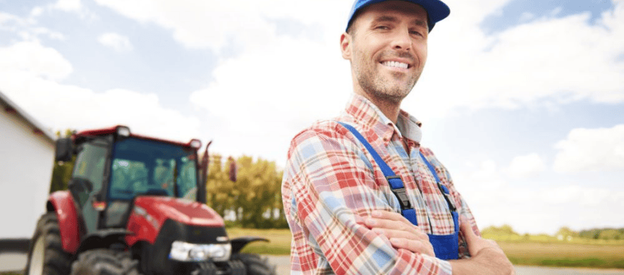 A farmer with his arms crossed stands next to a large red tractor after going through the agribusiness loans process.