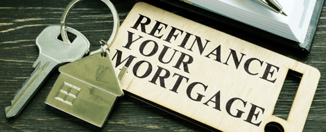 A close-up of a key with a keychain that reads “Refinance Your Mortgage” lays on a table next to a book that highlights the refinancing benefits banks offer.