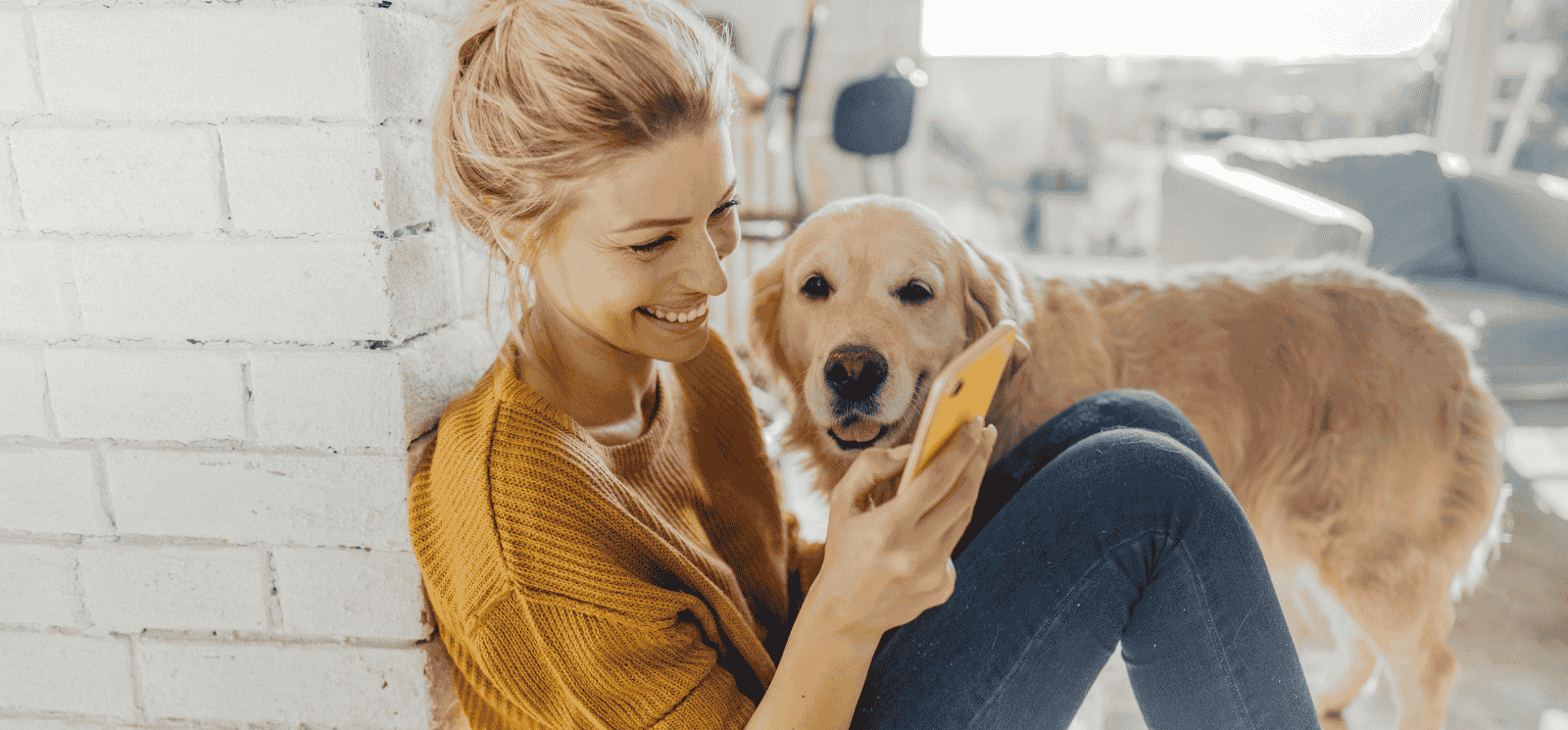 Woman smiling at her phone while sitting next to her golden retriever dog
